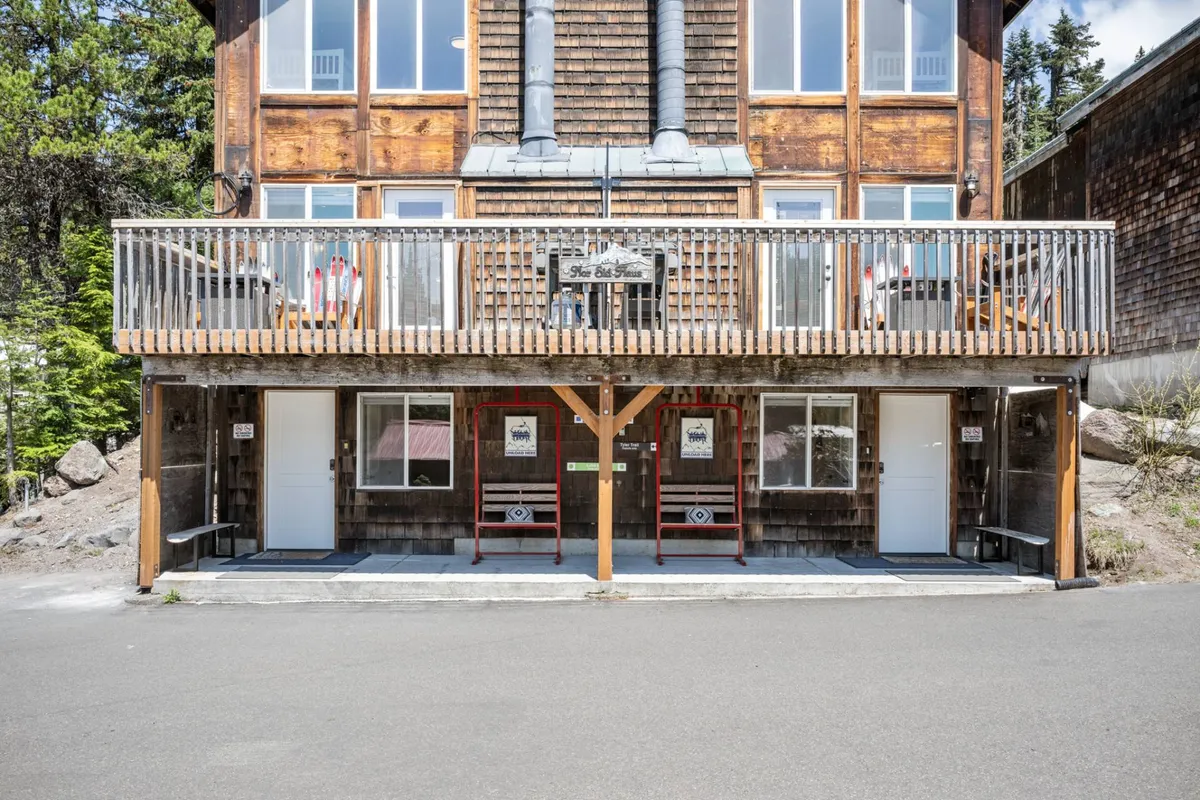 The exterior of Nor Ski Haus A, featuring a wooden balcony, large windows, two entrance doors, and visible chimneys. The scene suggests opportunities for gatherings on the balcony, enjoying mountain air, and relaxing after adventures.