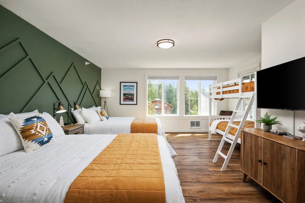 A bright, family-friendly bedroom featuring two bunk beds, a wooden dresser, and large windows that let in plenty of natural light. The playful arrangement and ample sleeping space make it ideal for children or teens. The room feels spacious and inviting, with decor that signals group bonding and relaxed fun.