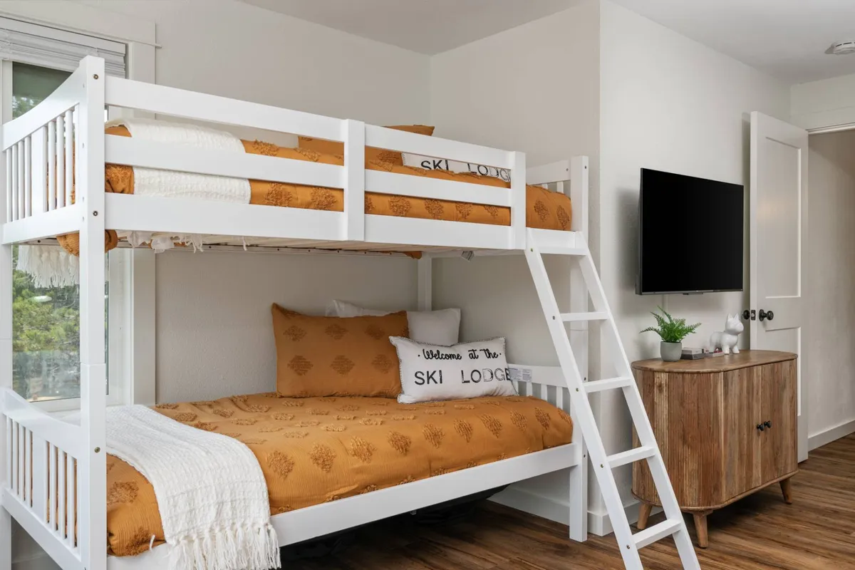 A cheerful bunk bedroom with multiple beds, decorative pillows, a television, and a wooden dresser. The setup provides ample space for sleeping and relaxing, with a TV for movie marathons or gaming sessions.