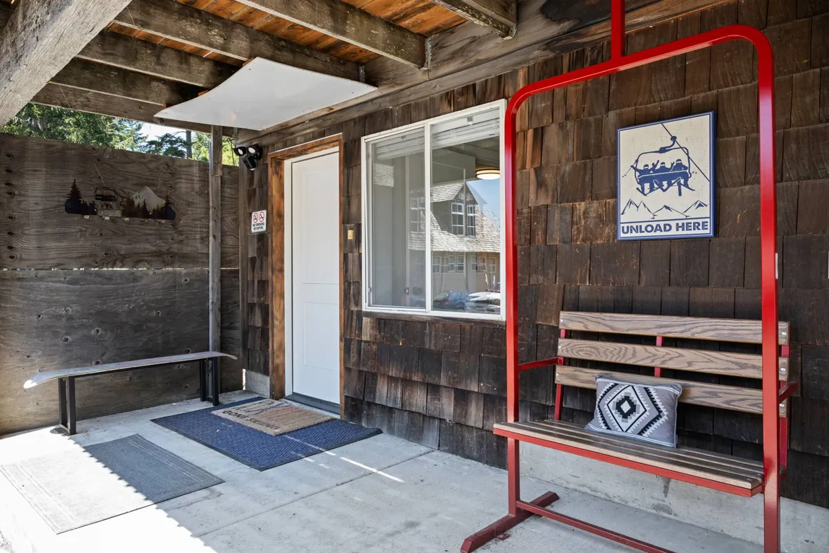 This exterior image shows a red swing bench set against inviting wooden wall paneling, with a welcoming 'UNLOAD HERE' sign. The scene evokes the first moments of arrival, suggesting both connection to the outdoors and a communal gathering spot before heading inside.