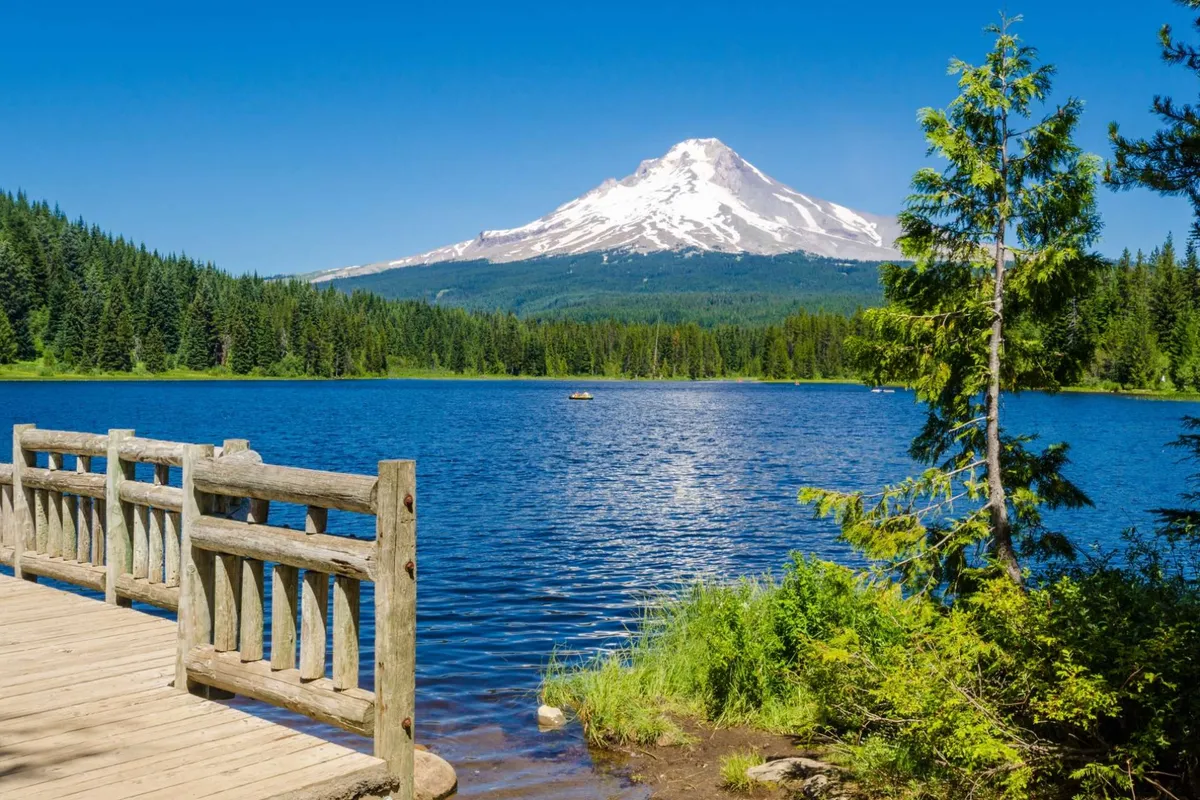A view-focused image showing a calm lake reflecting a mountain peak, with a wooden dock extending into the water and a lush forest all around. The peaceful atmosphere invites moments of quiet and reflection.