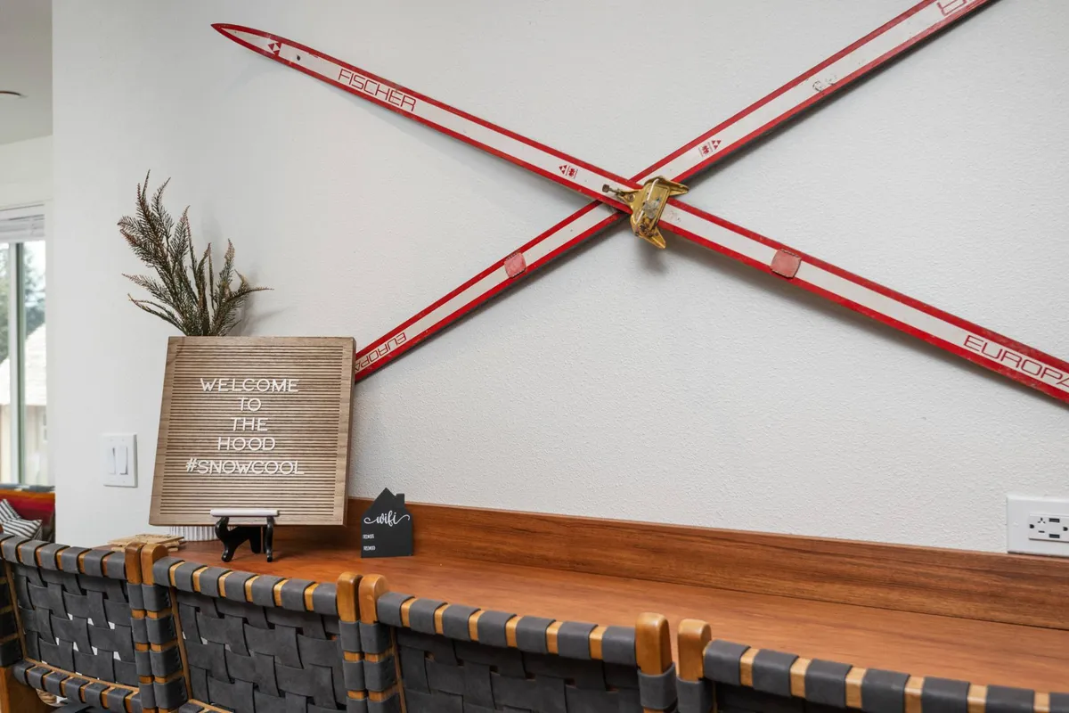 A warm, inviting interior with crossed skis on the wall, a 'welcome' sign, and wooden bar seating. The space is designed for socializing and relaxing after a day outside, capturing the cozy post-adventure atmosphere.