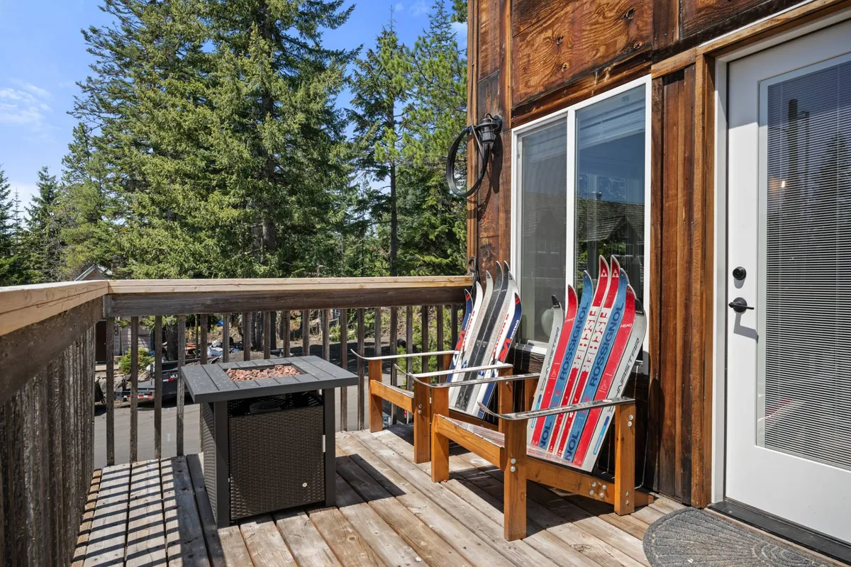 A view of a wooden deck featuring a cozy fire pit at its center, surrounded by ski equipment and natural tree cover. The setup invites guests to gather around the warmth, ideal for evening relaxation or enjoying the mountain atmosphere after a day outdoors.