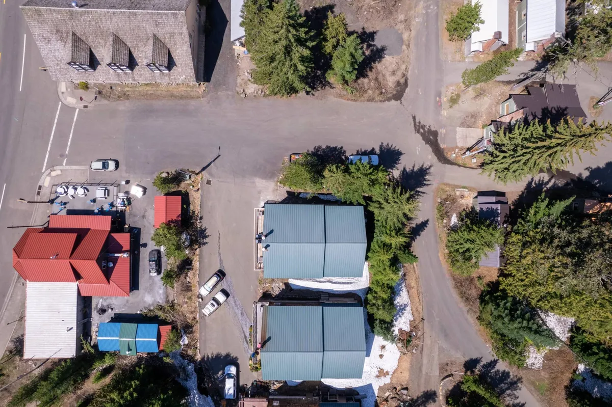 A lively exterior scene showing red roofs, green trees, and a crossroads in the heart of town. The image captures the energy of a mountain community, hinting at walkable access to shops, cafes, and local gathering spots amid scenic surroundings.