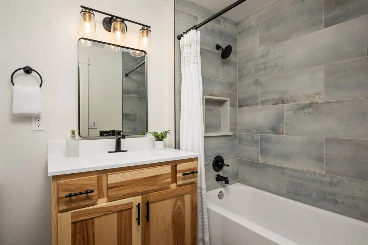 A stylish full bathroom featuring a natural wood vanity, a large mirror with modern light fixtures, and a bathtub with a tiled surround. The space feels serene and perfect for unwinding after a day of adventure.